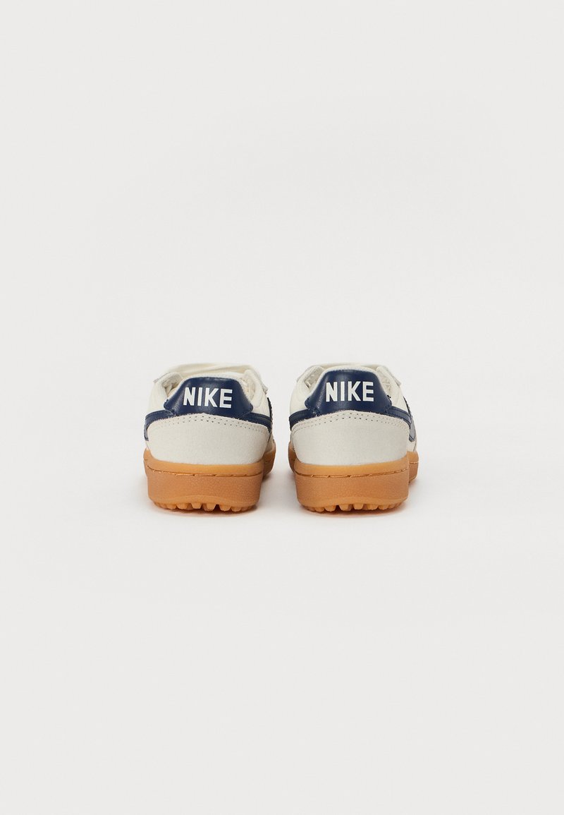 Zapatillas Nike con parte superior de color crema y acentos en azul marino, textura suave y suela de goma. Incluye el logo en el talón.