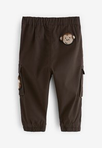 Braune Cargo-Hose mit dehnbarem Bund, seitlichen Taschen und einem aufgestickten Affengesicht auf der Vorderseite. Glattes Material mit elastischen Bündchen.