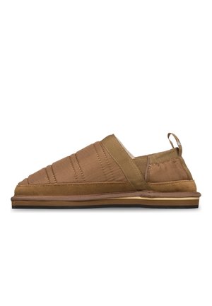 Brauner Slipper mit gesteppter Oberseite, elastischem Seitendetail, Wildlederbesatz und flacher Gummisohle, seitlich auf weißem Hintergrund betrachtet.