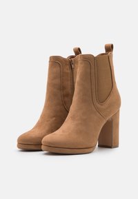 Ruskeat mokkanahkaiset nilkkurit, joissa on korkea paksu korko, joustavat sivupaneelit ja vetoketjusuljenta. Sileä pinta ja pyöreä kärki.