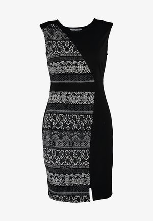 Czarna i biała sukienka bez rękawów z wzorzystą tkaniną z jednej strony, gładką czarną z drugiej; stylizowana z czarnymi rajstopami i błyszczącymi botkami za kostkę.