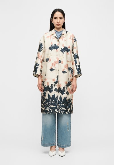 Manteau léger de couleur crème avec des motifs floraux et feuillus en bleu marine et rose pâle. Il présente une fermeture à boutons, des manches surdimensionnées et des poches.