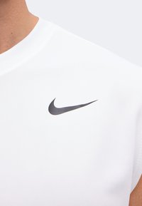 Gros plan d'une personne portant un haut de sport blanc avec un logo Nike Swoosh noir sur la poitrine.