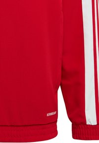 Chaqueta deportiva roja hecha de tejido suave, con franjas blancas a lo largo de las mangas y un pequeño logo "AEROREADY" en el dobladillo.