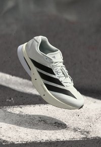 Leichter Laufschuh mit weißem Strick-Obermaterial, drei schwarzen Streifen und einer geschwungenen Sohle für verbesserte Leistung.