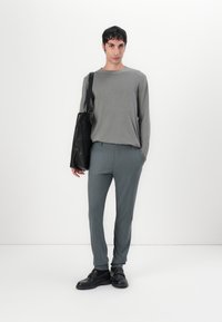 Grijze langemouwen top, taps toelopende lichtgrijze gestreepte broek, zwarte slingback schoenen en zwarte tote bag. Effen achtergrond.