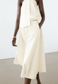 Haut en tissu côtelé de couleur crème avec un design asymétrique, associé à un short large et fluide plissé. Texture subtile et coupe décontractée.