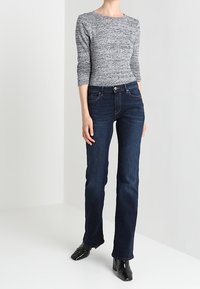 Šedý texturovaný top s dlouhým rukávem v kombinaci s tmavě modrými džíny rovného střihu. Džíny mají klasický pětikapsový design a stříbrný knoflík.