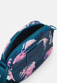 Borsa a pochette floreale nei toni del teal e del rosa, con logo in gomma, chiusura a zip e tracolla regolabile. Interno testurizzato per una conservazione sicura.