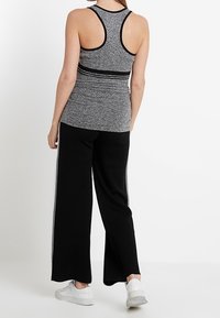 Grå sporttopp i racerback-design med svarta detaljer, tillsammans med löst sittande svarta byxor med sidostreck och vita sneakers.