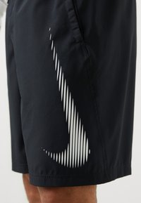 Shorts de bain noirs avec une texture lisse, présentant un design graphique argenté de lignes verticales sur le côté. Ceinture élastique, coupe décontractée.