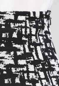 Falda de patrón en blanco y negro que presenta un tejido texturizado con un diseño geométrico, detalle de cremallera lateral y un corte ajustado.