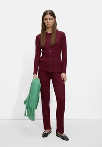 Prążkowany, bordowy sweter z guzikami, dopasowane spodnie oraz zielony szal z frędzlami. Czarne baleriny z srebrnymi ćwiekami dopełniają całość.