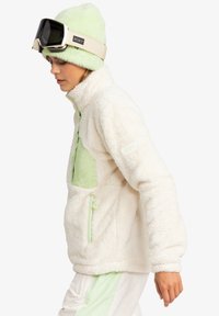 White fleece pullover with mint green accents, zip pocket, and a green beanie. Features a soft texture and casual, loose fit.