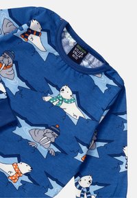 Blue organic cotton long-sleeve shirt featuring polar bears and walruses, with green and orange scarves, and a textured patterned background.