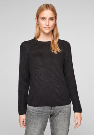 Pull en maille noir avec motif texturé, col rond et manches longues. Associé à un jean gris, souligné par un design minimaliste.