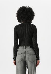 Top de manga larga de punto acanalado negro con silueta ajustada. Combinado con jeans de pierna ancha de talle alto en gris claro que cuentan con bolsillos traseros.