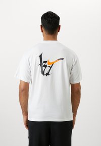 Witte t-shirt met korte mouwen van katoen, met een multikleurig logo in zwart, oranje en groen op de achterkant.
