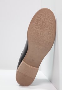 Schwarze Ledersohle eines Schuhs mit strukturierten Blumen- und Wirbelmustern. Brauner Gummihals und Zwischensohle, mit Größe 37 gekennzeichnet.