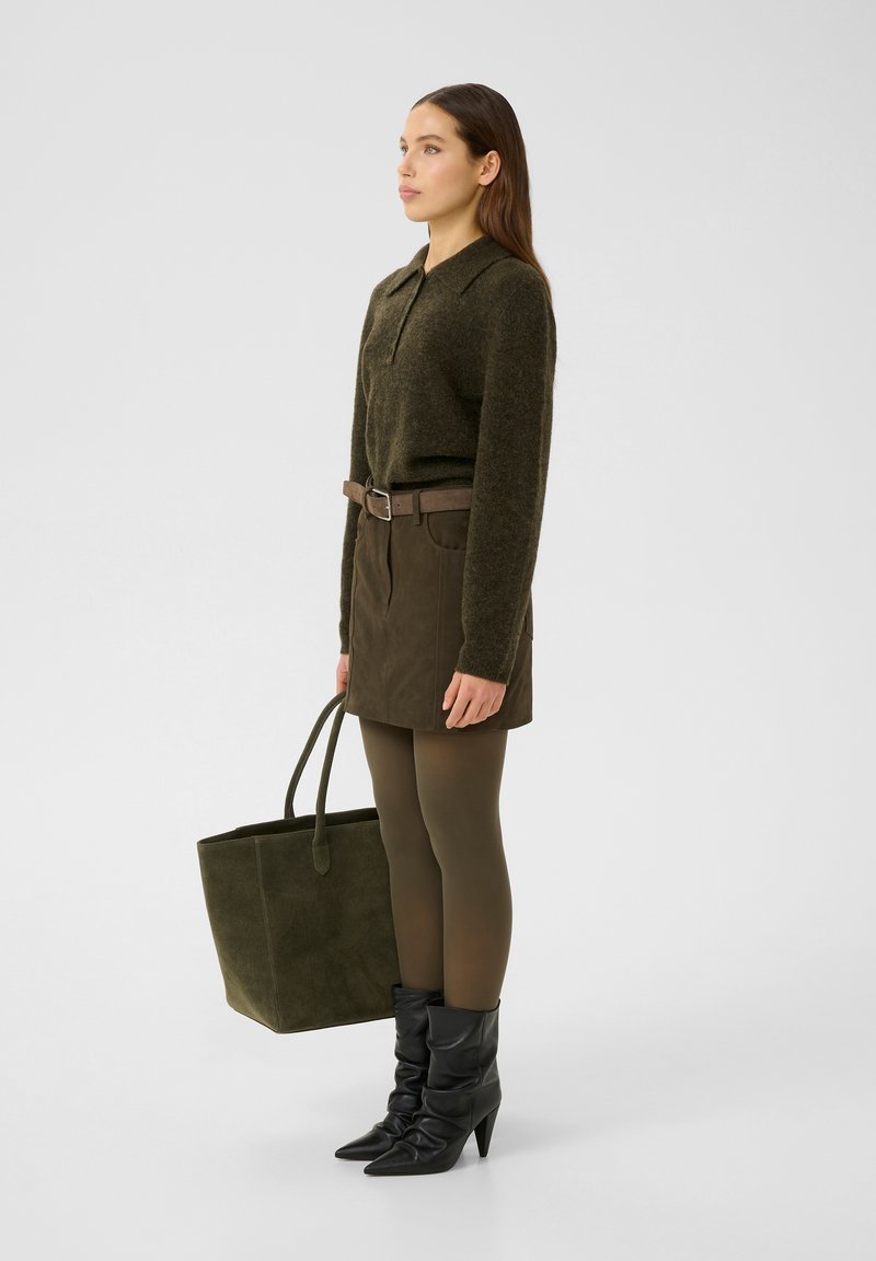 Olivenfarbener Strickpullover, braune Wildlederrock mit Taschen, olivgrüne Strumpfhosen, schwarze spitze Stiefeletten und eine dunkelgrüne Tasche.