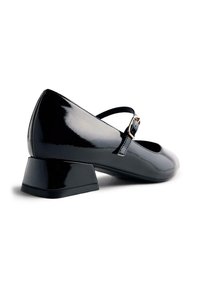 Scarpe con tacco a blocco in vernice nera, dalla punta arrotondata, con una sottile cinturina con una fibbia metallica sopra il collo del piede.