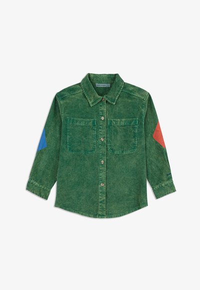 Camisa de pana verde con botones en el frente, dos bolsillos en el pecho y parches en los codos en azul y rojo en las mangas largas.