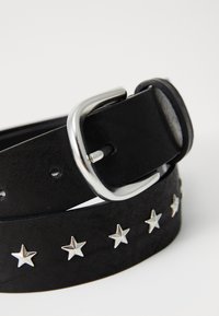 Ceinture en daim noir avec des clous en forme d'étoile argentés et une boucle en métal argenté. La ceinture est plate et légèrement texturée, avec plusieurs trous pour le réglage.