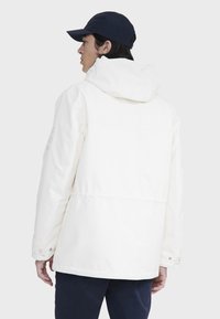 Hvid hættetrøje med et rent design, justerbar snor og trykknapper, parret med en marineblå kasket.