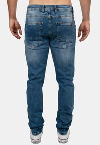 Blauwe denim jeans met een fitted ontwerp, vervaagde details en twee achterzakken. Gecombineerd met witte sneakers met een rode accent.