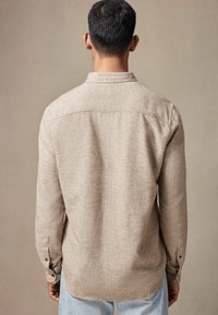 Lys brun, tekstureret skjorte med lange ærmer, rygpanel detalje og enkeltknap manchetter, båret med lyseblå jeans.