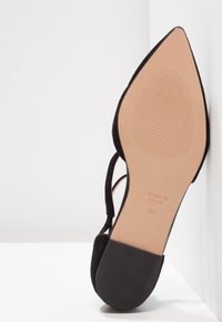 Chaussure noire en suède à bout pointu avec un design découpé, une semelle beige, et l'inscription en relief "MADE IN SPAIN" ainsi que la taille 37 sous la semelle.