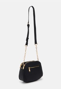 Sort pebret læder crossover taske med en rund form, to lynlåslommer og guldfarvede hardware detaljer. Justerbar rem inkluderet.