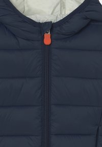 Marinblå puffjacka med huva, som har horisontella quiltade sektioner, en fullständig dragkedja med en orange dragflik och en vit innervaning.