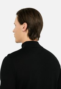 Maglione nero lavorato a maglia con colletto alto, design aderente, texture liscia e sottili coste sul colletto e sulle cuciture delle spalle.