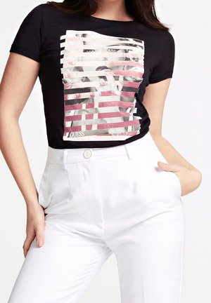 T-shirt noir à manches courtes avec un imprimé graphique comportant des rayures horizontales rose et blanche, superposées sur un visage. Associé à un pantalon blanc.
