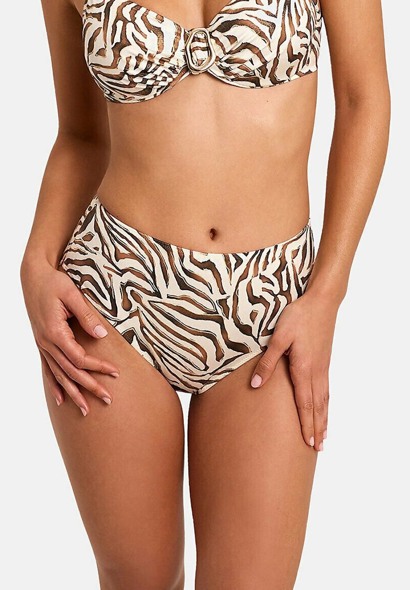 Femme portant un bikini imprimé zèbre marron et blanc avec un haut à armatures et un bas taille haute, debout les mains posées sur les hanches.