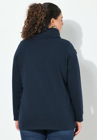 Top a maniche lunghe blu navy con colletto alto e bottoni laterali, realizzato in tessuto morbido con una vestibilità comoda.