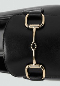 Zwarte leren schoen met een kenmerkende gouden hardwareaccent en een diamantvormige uitsnijding. Glad textuur met omlijnde stikseldetails.