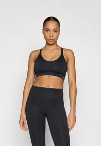 Black sports bra with a v-neck design, thin adjustable straps, and a wide elastic band. Worn with matching black high-waisted leggings.