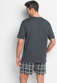 T-shirt gris à manches courtes avec un col rond, associé à un short à motifs avec un design à carreaux noir et gris. Texture de tissu lisse.