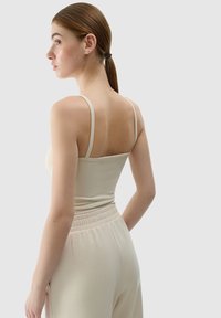 Top ajustado color beige claro con tirantes finos, que muestra una textura suave. Combinado con pantalones de tiro alto a juego que cuentan con una cintura elástica.