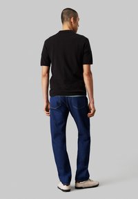 Polo nero con maniche corte, abbinato a jeans in denim blu. La vista dal retro mostra una texture liscia e semplici dettagli di cucitura.