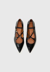 Chaussures en cuir verni noir à bout pointu avec des découpes, présentant un design à brides croisées et une semelle intérieure beige.