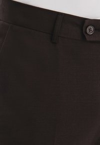 Brązowe spodnie wizytowe o gładkiej fakturze, z w�ąskim paskiem w talii i pojedynczym zapięciem na guzik, widoczne detale przeszyć.