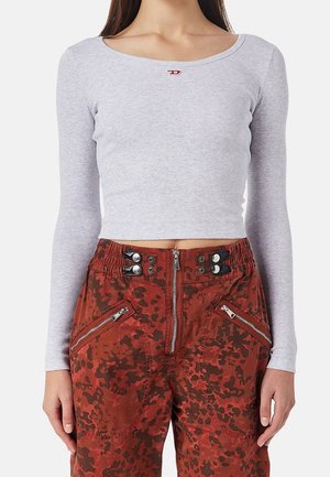 Kobieta nosząca dopasowany jasnoszary crop top z długim rękawem i czerwone spodnie moro z wysokim stanem, z zamkami błyskawicznymi z przodu i guzikami.