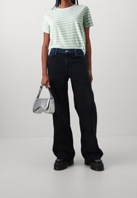 Pruhované zeleno-bílé tričko spárované s volnými černými džíny, doplněné stříbrnou kabelkou a masivními černými platformovými botami.