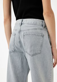 Jeans de mezclilla gris claro con un diseño de cintura alta, que cuentan con dos bolsillos traseros y un ajuste relajado. La tela tiene una ligera textura.