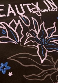 Tela negra con diseños florales en tonos rosa y azul, que presenta un texto en relieve "BELLEZA EN LA SIMPLICIDAD". La textura es suave con un acabado vibrante y brillante.