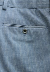 Tissu bleu clair à fines rayures avec une poche arrière passepoilée boutonnée, passants de ceinture et détails de couture verticale sur un pantalon sur mesure.