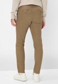 Lichtbruine slim-fit broeken van zachte stof, met een platte voorkant en achterzakken met knopen, gestyled in een casual look en gecombineerd met witte schoenen.
